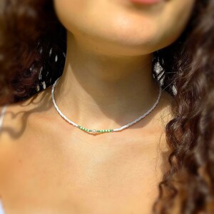 May include: A white beaded necklace with a single pearl and green beads.