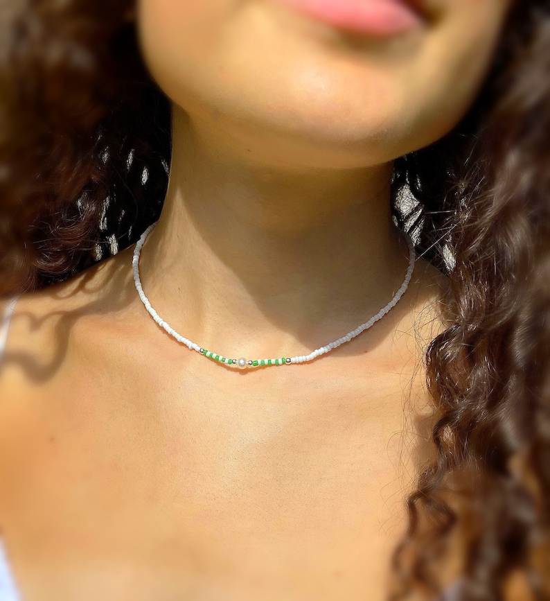May include: A white beaded necklace with a single pearl and green beads.