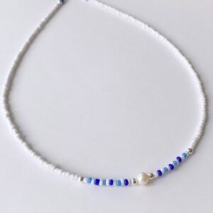 May include: A white beaded necklace with a single pearl accent and blue and light blue beads.