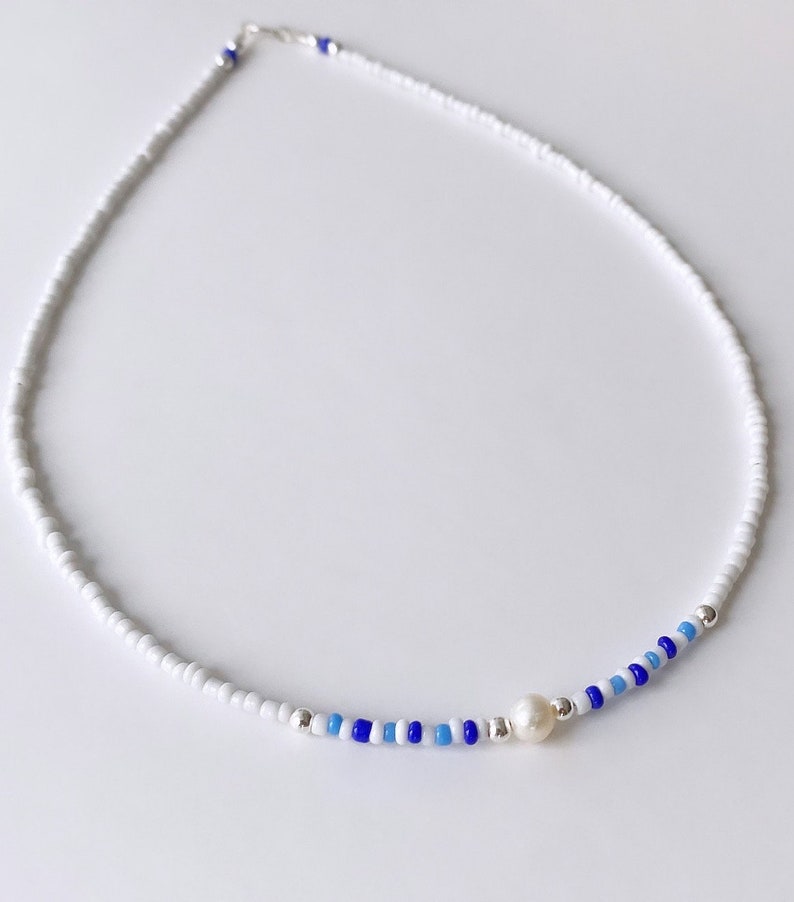 May include: A white beaded necklace with a single pearl accent and blue and light blue beads.