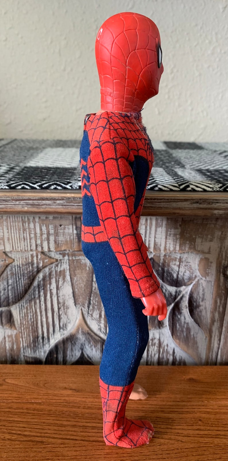 K&ouml;nnte beinhalten: Eine Vintage-Spider-Man-Actionfigur. Die Figur ist haupts&auml;chlich rot und blau, mit einer roten Maske und einem blauen K&ouml;rper. Das Kost&uuml;m hat ein Spinnennetz-Design. Die Figur steht auf einer Holzoberfl&auml;che.