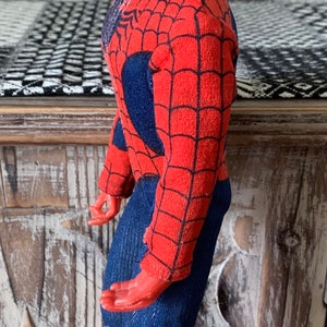 K&ouml;nnte beinhalten: Eine Vintage-Spider-Man-Actionfigur. Die Figur ist haupts&auml;chlich rot mit einem schwarzen Netzmuster und blauen Akzenten. Der Kopf ist rot mit wei&szlig;en Augenlinsen. Die Figur steht auf einer Holzoberfl&auml;che.
