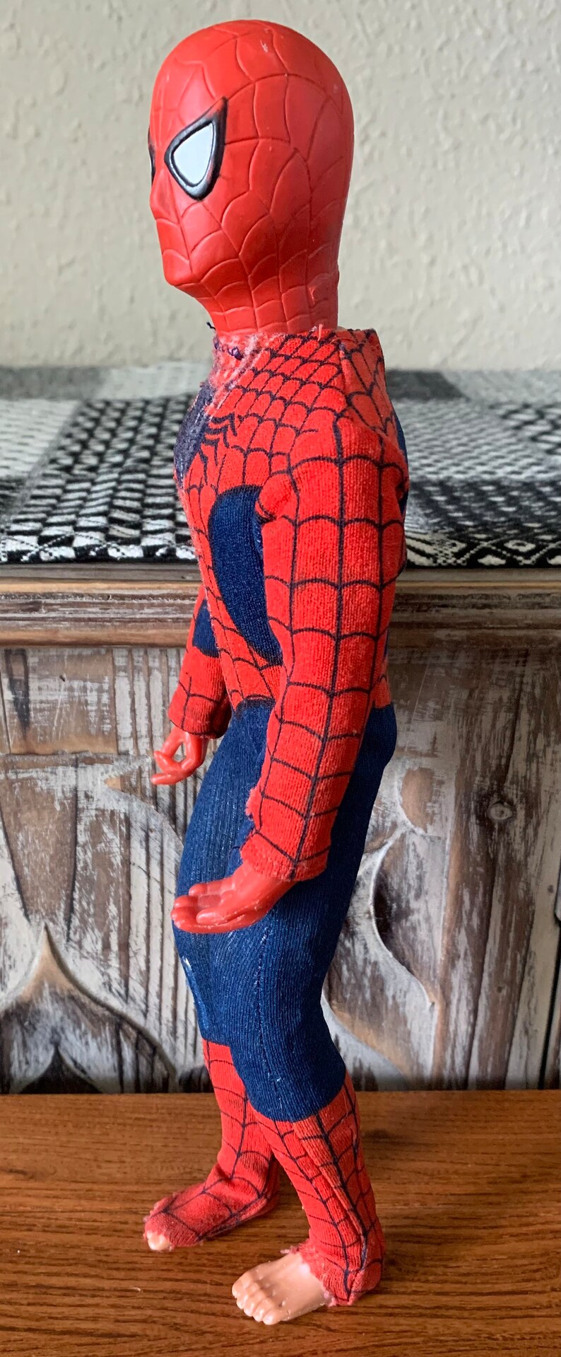 K&ouml;nnte beinhalten: Eine Vintage-Spider-Man-Actionfigur. Die Figur ist haupts&auml;chlich rot mit einem schwarzen Netzmuster und blauen Akzenten. Der Kopf ist rot mit wei&szlig;en Augenlinsen. Die Figur steht auf einer Holzoberfl&auml;che.