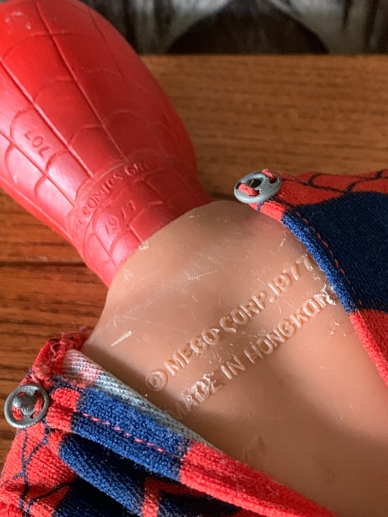 K&ouml;nnte beinhalten: Vintage Spider-Man-Actionfigur mit rotem und blauem Kost&uuml;m mit Spinnennetz-Muster. Der Kopf der Figur ist rot, der K&ouml;rper ist hautfarben. Der Text auf der Figur lautet: "MEGO CORP. 1977 MADE IN HONGKONG".