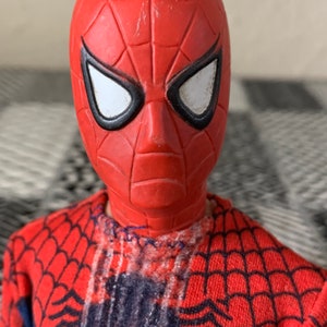 K&ouml;nnte beinhalten: Nahaufnahme einer Spider-Man-Actionfigur. Der Kopf der Figur ist rot mit einer strukturierten Oberfl&auml;che und wei&szlig;en Augenlinsen, die schwarz umrandet sind. Das rot-blaue Kost&uuml;m der Figur weist ein Netzmuster auf.