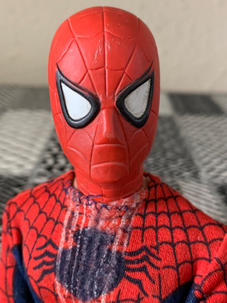 K&ouml;nnte beinhalten: Nahaufnahme einer Spider-Man-Actionfigur. Der Kopf der Figur ist rot mit einer strukturierten Oberfl&auml;che und wei&szlig;en Augenlinsen, die schwarz umrandet sind. Das rot-blaue Kost&uuml;m der Figur weist ein Netzmuster auf.