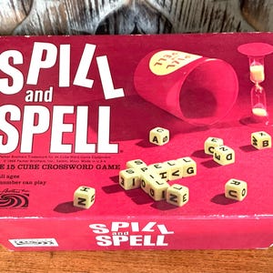 May include: A red box game called "Spill and Spell: The 15 Cube Crossword Game". The box features a red cup with a yellow lid and an hourglass. The game is for all ages and any number of people can play.