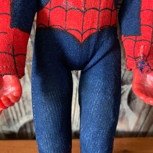 K&ouml;nnte beinhalten: Eine Vintage-Spider-Man-Actionfigur mit einem rot-blauen Kost&uuml;m mit Spinnennetz-Muster. Die Figur hat rote H&auml;nde und einen blauen Overall. Das Kost&uuml;m weist Gebrauchsspuren auf, was seinen Vintage-Reiz verst&auml;rkt. Die Figur ist ein Sammlerspielzeug.