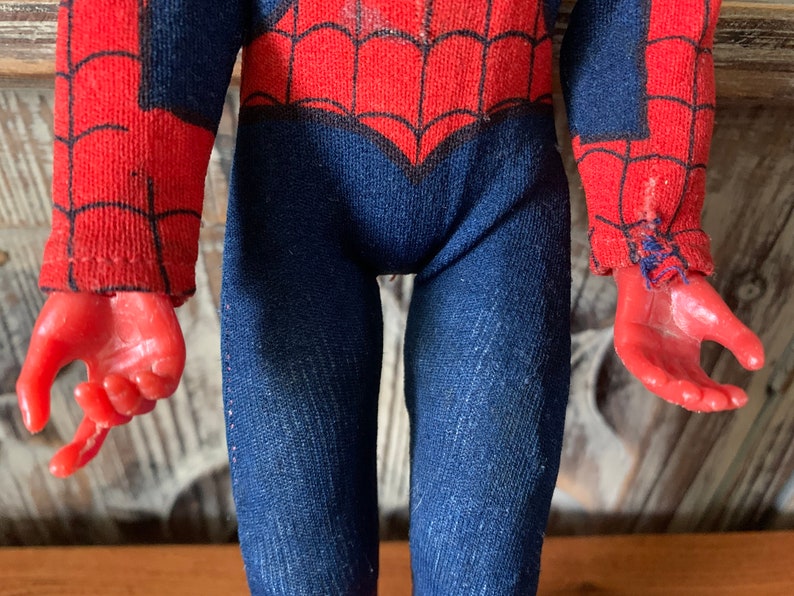 K&ouml;nnte beinhalten: Eine Vintage-Spider-Man-Actionfigur mit einem rot-blauen Kost&uuml;m mit Spinnennetz-Muster. Die Figur hat rote H&auml;nde und einen blauen Overall. Das Kost&uuml;m weist Gebrauchsspuren auf, was seinen Vintage-Reiz verst&auml;rkt. Die Figur ist ein Sammlerspielzeug.