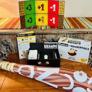 May include: A board game set with a colorful game board, cards, and a box labeled "Poetry for Neanderthals." An inflatable club and an hourglass are also present. The game board has point values and team names.