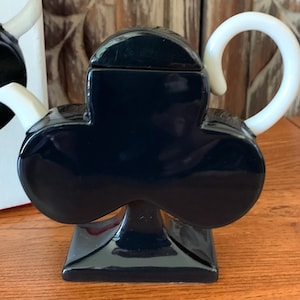 May include: Black ceramic teapot shaped like a clover with a white handle and spout.