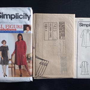 May include: A Simplicity 7423 sewing pattern packet for full figure solutions, including a front envelope with illustrations of three garments, a brown paper pattern envelope, and a white instruction sheet with line drawings of dresses and pants.