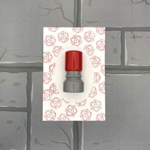 May include: A red and gray ink stamp with a design of a single die with the number one on it. The stamp is on a white background with a repeating pattern of red dice.