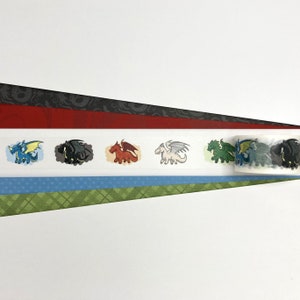 May include: A roll of washi tape with a repeating pattern of colorful cartoon dragons. The tape is on a white background and has a red, black, and green striped pattern underneath.