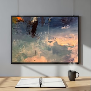 May include: Abstract art print in a black frame. The artwork features a textured, colorful design with shades of blue, orange, and white. A black coffee mug and an open notebook with a spiral binding sit on a wooden desk.