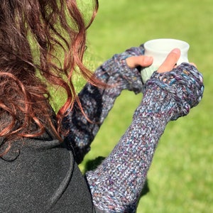 May include: A pair of fingerless gloves in a multi-colored yarn with a speckled pattern. The gloves are knitted and have a loose, textured stitch.