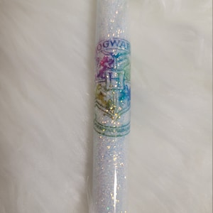 May include: A white glitter wand with a rainbow Hogwarts crest logo.