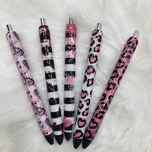 May include: Five black and white pens with pink glitter and different patterns, including hearts, stripes, and animal print.