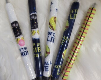 May include: Five different softball-themed pens with glitter and various designs. The pens feature a softball, a baseball, and text that says "Softball Life", "Ball Life", "Softball", "Dirt On It", and "FTB/MOI".