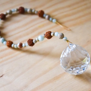 May include: A crystal suncatcher with a beaded chain. The chain is made of brown, beige, and light blue beads.
