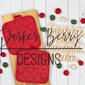 May include: Two red quilted pot holders with the text "Parker Berry Designs" on a wooden cutting board. The background is a white woodgrain surface with decorative pom-poms in red, white, and green.