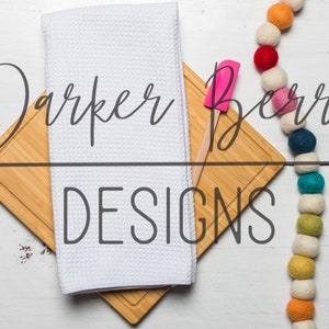 May include: A white kitchen towel and a wooden cutting board with a pink spatula on top. The text "Parker Berry Designs" is written in black cursive on the cutting board. A colorful garland of felt balls hangs on the right side of the image.