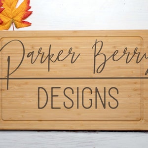 Könnte beinhalten: Ein Holzbrett zum Schneiden mit dem eingravierten Text "Parker Berry Designs". Das Brett ist von Herbstblättern umgeben.