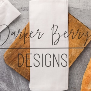 May include: A white kitchen towel with the text "Parker Berry Designs" on a wooden chopping board with a baguette beside it.