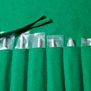 May include: A green felt carrying case with a drawstring closure holds a set of tuning forks in individual plastic sleeves.