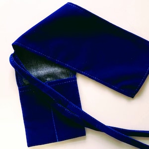 May include: A blue velvet pouch with a long strap and a tassel. The pouch is closed and the strap is tied in a knot.