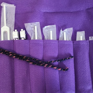May include: A purple felt carrying case with a black and red cord. The case has multiple pockets for holding tuning forks. The tuning forks are visible inside the pockets.