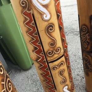 Pode incluir: Um conjunto de três tubos de bambu de madeira com entalhes intrincados e desenhos pintados em tons de marrom, branco e vermelho. Os tubos são decorados com padrões em espiral e linhas em ziguezague.