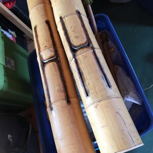 Pode incluir: Dois tubos de bambu de madeira com recortes e marcas. Os tubos estão em um recipiente de plástico azul.