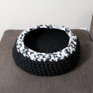 May include: A black and white crocheted pet bed. The bed is round and has a white rim.