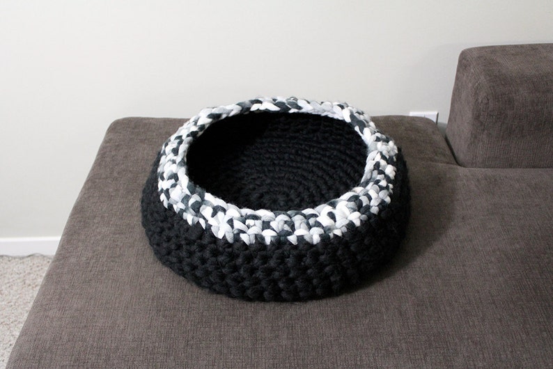 May include: A black and white crocheted pet bed. The bed is round and has a white rim.