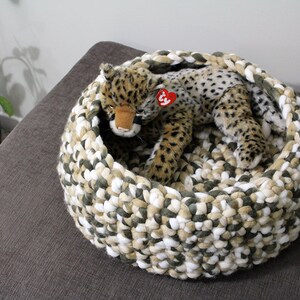 May include: A crocheted pet bed in shades of white, beige, and green with a stuffed cheetah toy inside.
