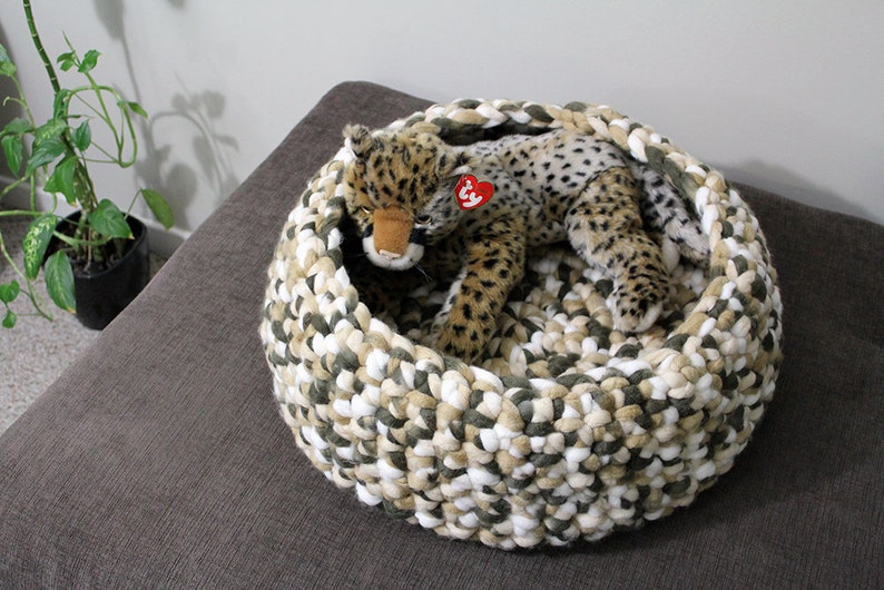May include: A crocheted pet bed in shades of white, beige, and green with a stuffed cheetah toy inside.