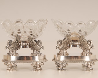 May include: A pair of silver and crystal serving dishes with swan-shaped feet and a decorative base. The dishes are clear and have a cut-glass design.
