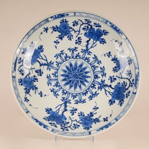 May include: A large, white porcelain plate with a blue and white floral design. The plate has a central medallion with a stylised flower and a border of repeating floral motifs.