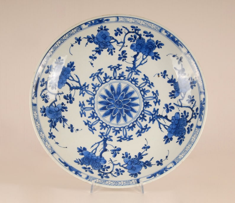 May include: A large, white porcelain plate with a blue and white floral design. The plate has a central medallion with a stylised flower and a border of repeating floral motifs.