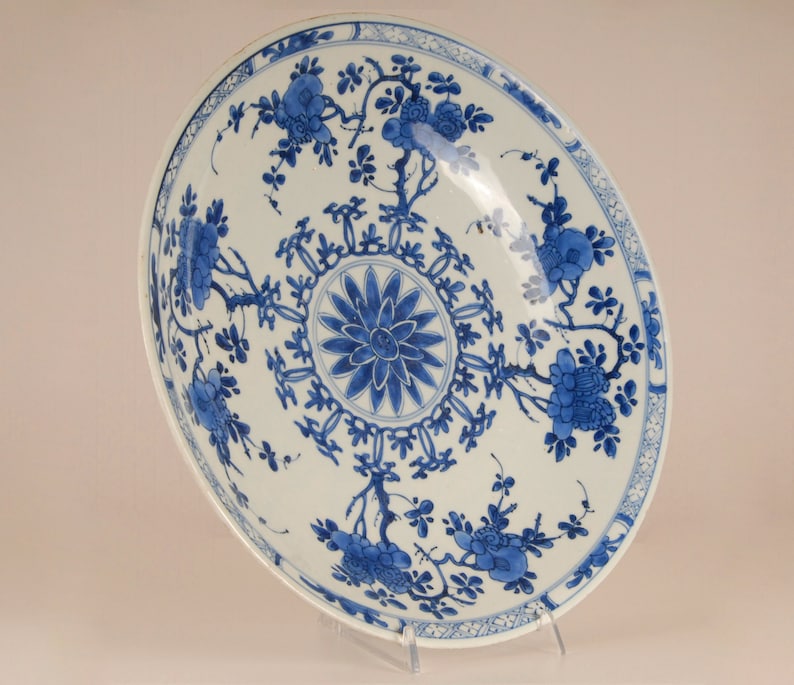 May include: A large, white porcelain bowl with a blue and white floral design. The bowl features a central medallion with a stylised flower and a border of repeating floral motifs.