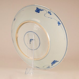 May include: A white porcelain plate with a blue and white floral design. The plate is on a clear plastic stand.