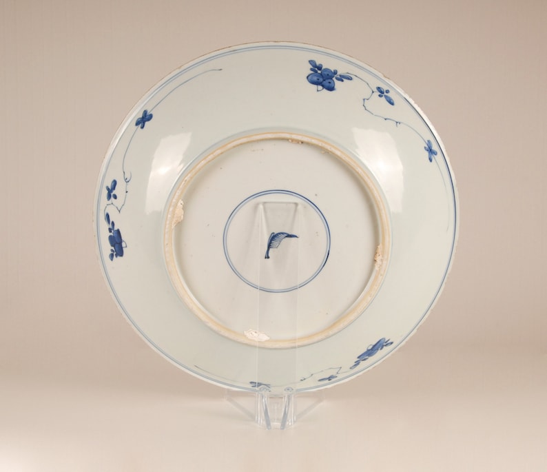 May include: The reverse of a white porcelain plate featuring a blue floral design. The plate has a raised rim and a slightly scalloped edge.