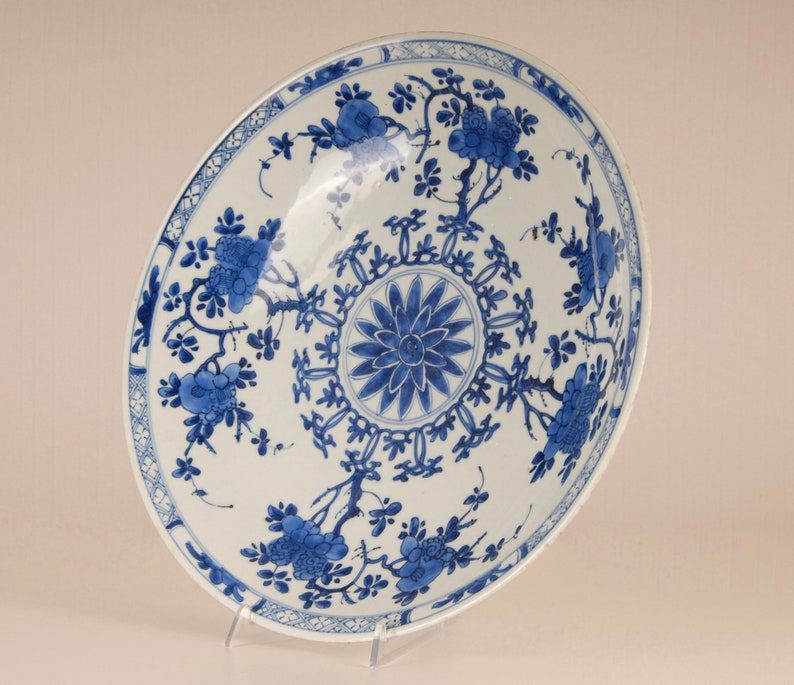 May include: A large, white porcelain plate with a blue and white floral design. The plate has a central medallion with a stylised flower and a border of repeating floral motifs.