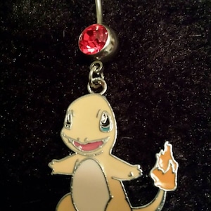 May include: A silver belly button ring with a red gem and a Charmander charm. The Charmander is orange, tan, and white with a flame tail. The gem is a bright red color.