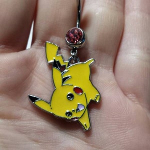 May include: A silver belly button ring featuring a yellow Pikachu charm. The charm has black and red accents. The top ball and the charm's dangling gem are both silver. The charm is a cartoon character.