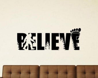 Könnte beinhalten: Schwarzer und weißer Vinyl-Wandaufkleber mit dem Wort "BELIEVE" in großen Buchstaben. Der Buchstabe "E" wird durch einen Fußabdruck ersetzt. Eine Silhouette von Bigfoot geht vor dem Buchstaben "B" entlang.