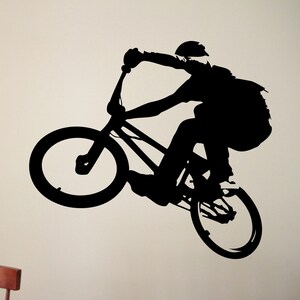 May include: Silhouette of a person riding a BMX bike, performing a trick with the front wheel in the air.