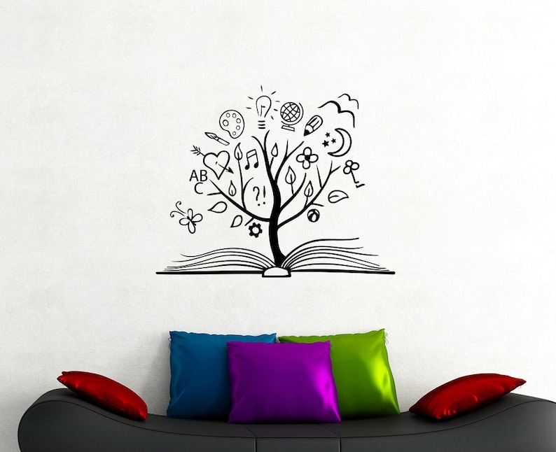 May include: Black and white illustration of a tree growing out of an open book. The tree is decorated with various symbols including a light bulb, musical notes, a heart, a flower, and letters. The illustration is on a white wall above a black couch with colorful throw pillows.