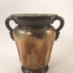 May include: A brown and green ceramic vase with two handles. The vase has a mottled glaze with shades of brown, orange, and yellow.